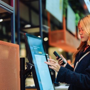 Women in casual clothing paying using automatic payment machine and smartphone.