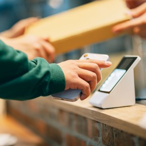 In the restaurant, a woman uses her smartphone to make a payment with the cashier. She scans the QR code using a card reader to complete a convenient contactless payment. At the same time, the cashier hands over the purchased pizza to the customer.