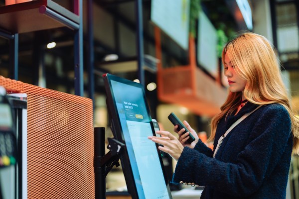 Women in casual clothing paying using automatic payment machine and smartphone.